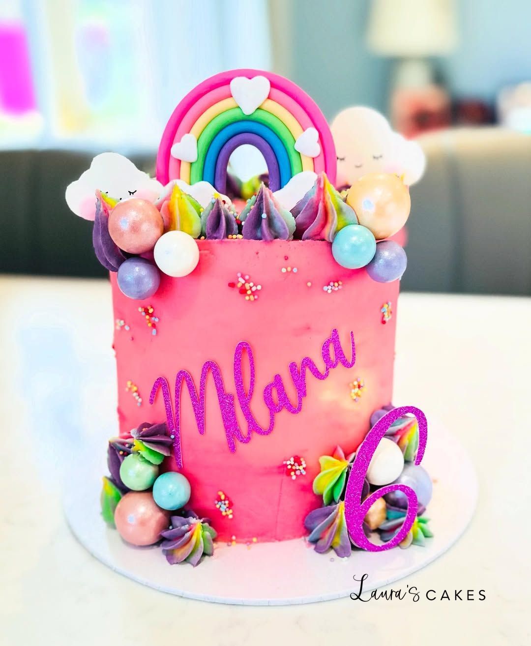Celebration cake: A pink cake with a rainbow theme and a name on it